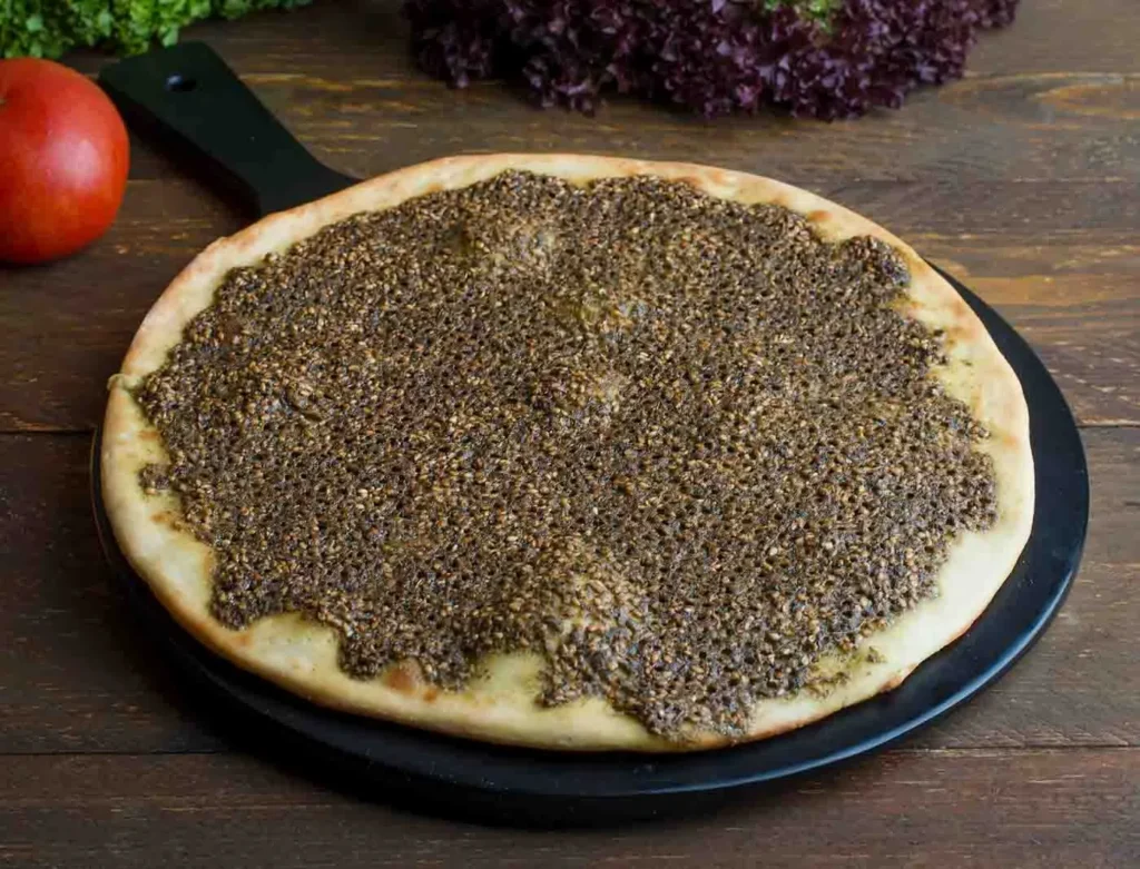Man'ouché au zaatar, pâte ronde avec épice zaatar en surface, sur planche en bois.