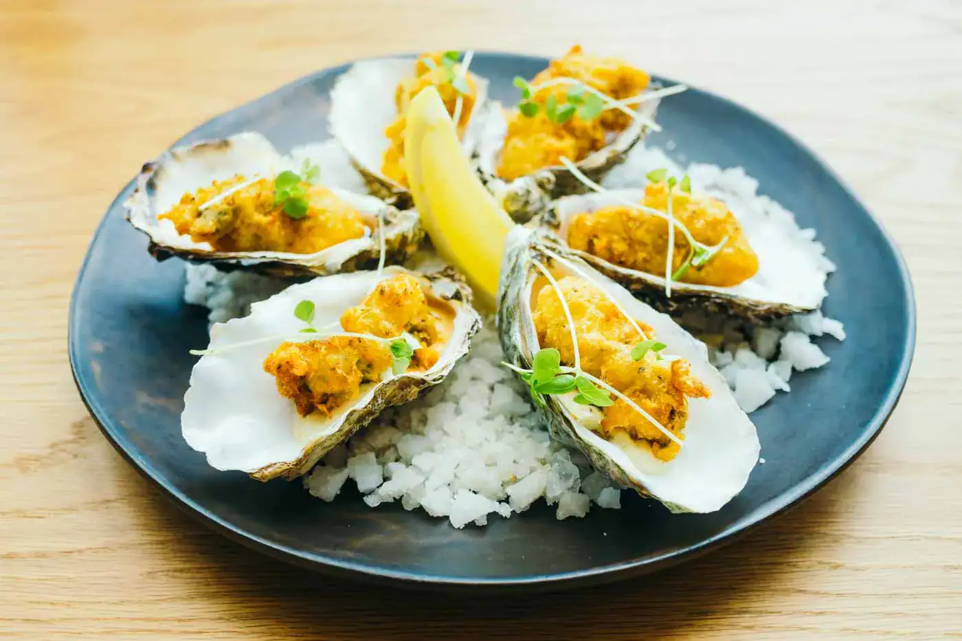 Huîtres gratinées avec sauce au vin blanc, garnies de verveine, servies sur un lit de sel de mer sur une assiette bleue.