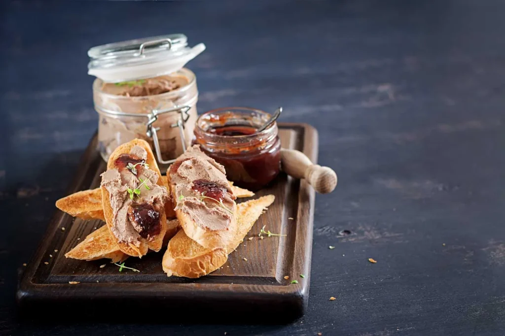 Terrine de foie gras tranchée avec confiture de figues, sur planche en bois, accompagnée de pain grillé.