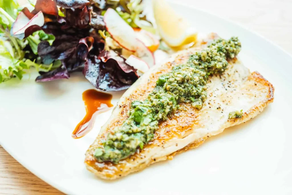 Poisson en croûte d'herbes avec sauce au citron et salade verte sur assiette blanche.