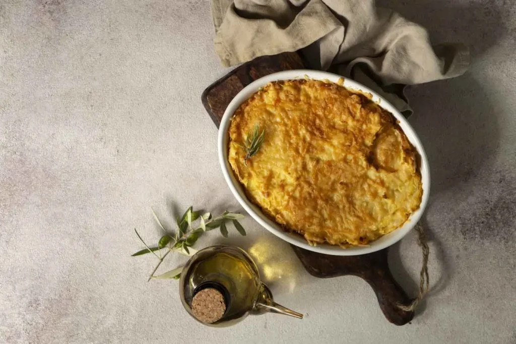 Gratin dauphinois dans un plat en céramique, avec une croûte dorée et du fromage fondu, sur un fond en pierre et lin beige.