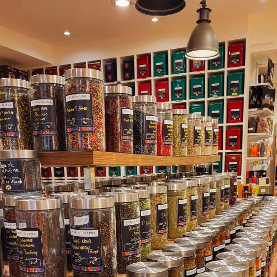 Pot d'épices multicolores en verre avec couvercle métallique, rangés sur étagère en boutique d'épicerie fine.