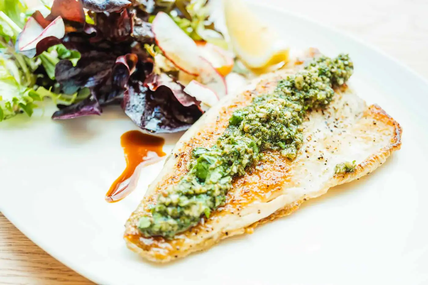 Filet de poisson avec sauce verte aux herbes, salade verte et vinaigrette sur assiette blanche.