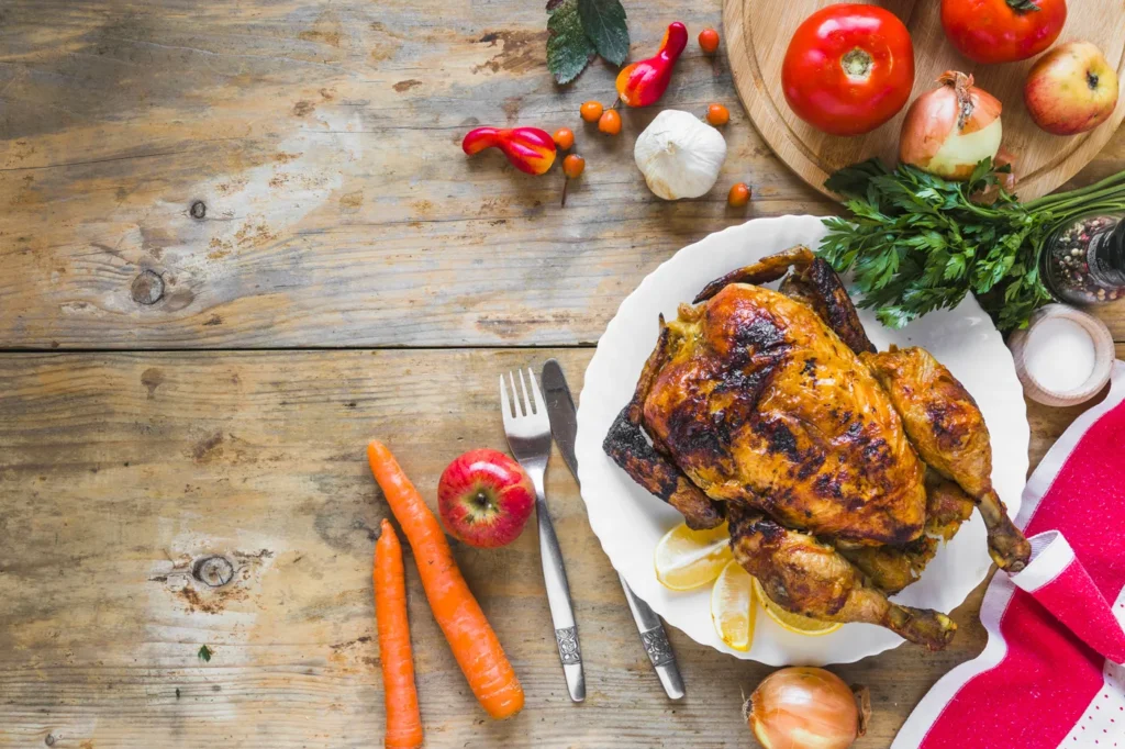Poulet rôti doré avec carottes, oignons, tomates et herbes sur une table en bois.