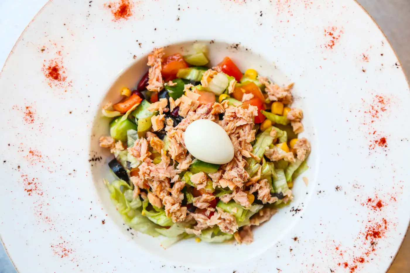 Salade Niçoise au Mélange 5 Baies Salade de thon, céleri, carottes, maïs, œuf dur, sur assiette blanche avec épices rouges autour.