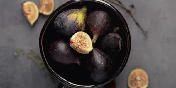 Figues fraîches dans un bol noir, avec quelques figues coupées, texture douce et couleur violette foncée.