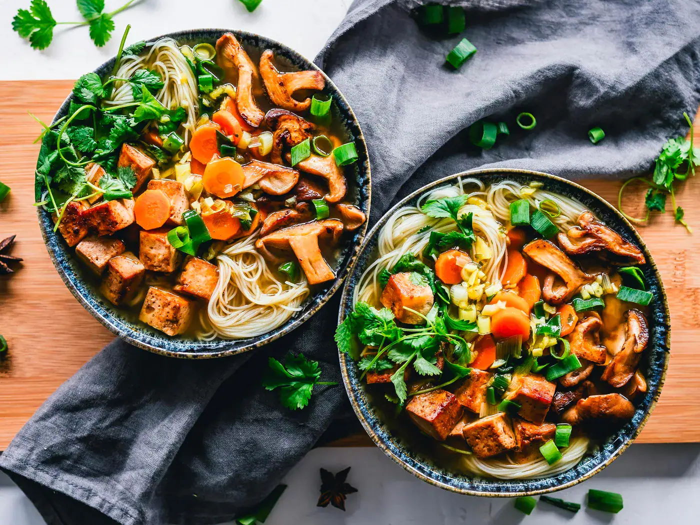 Tofu Mariné et Grillé au Sésame Kimchi Soupe de nouilles avec légumes, tofu, carottes, champignons, et ciboulette dans deux bols en céramique.