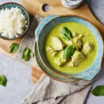 Poulet en sauce verte avec basilic, servi avec riz blanc, dans un bol en céramique sur une nappe en lin beige.